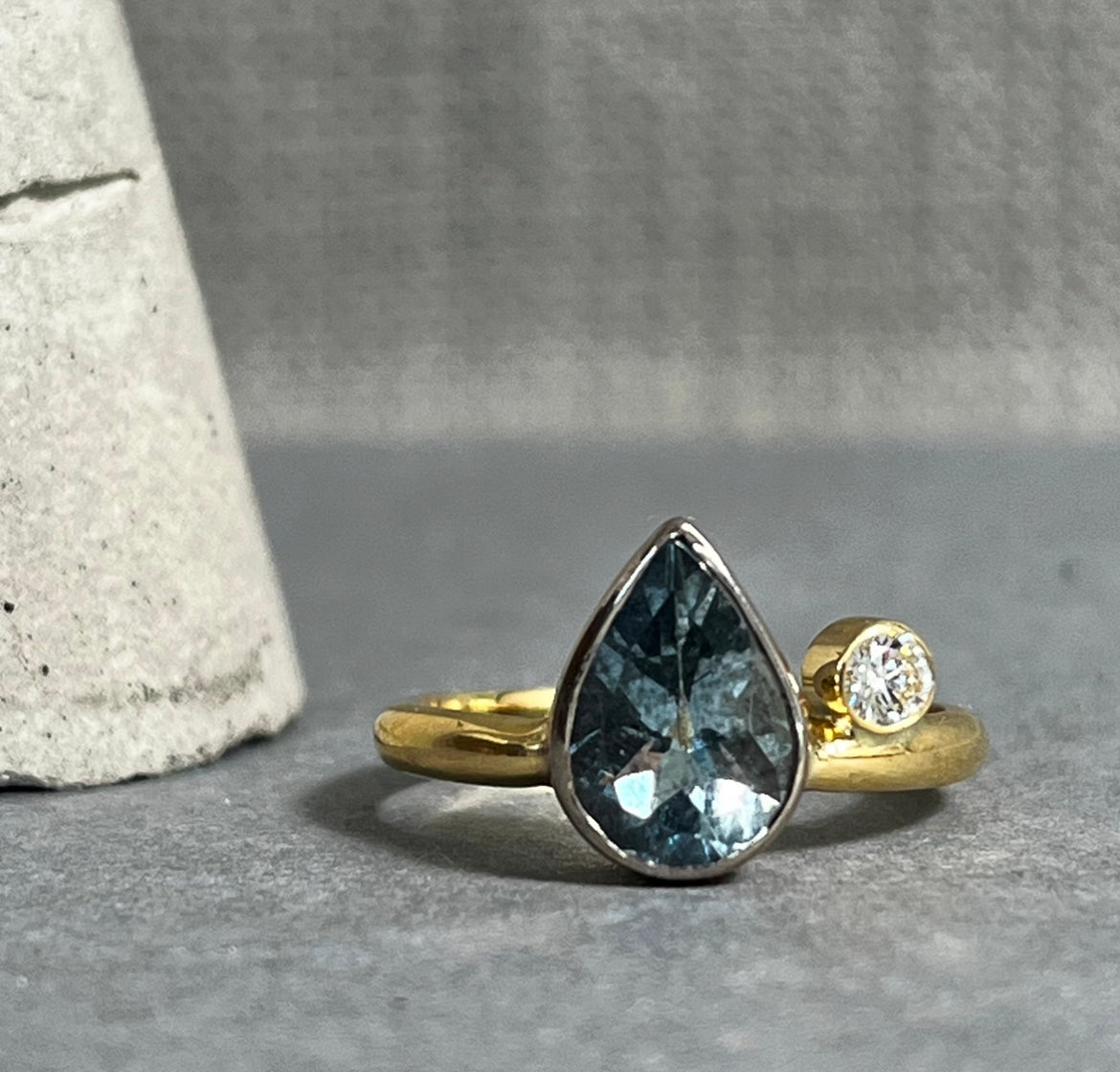 Gold ring with a tear drop shaped gem stone in blue and a small round diamond